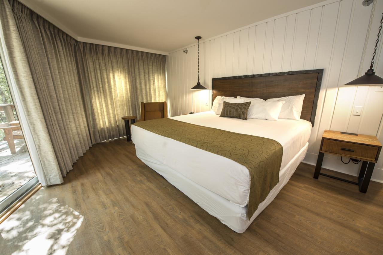 A view of the sleeping area with a king bed and armchair in the standard suite at the Ozark Folk Center State Park